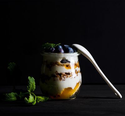 Yogurt and oat granola with jam, blueberries and mint leaves in glass jar on black background, selective focus